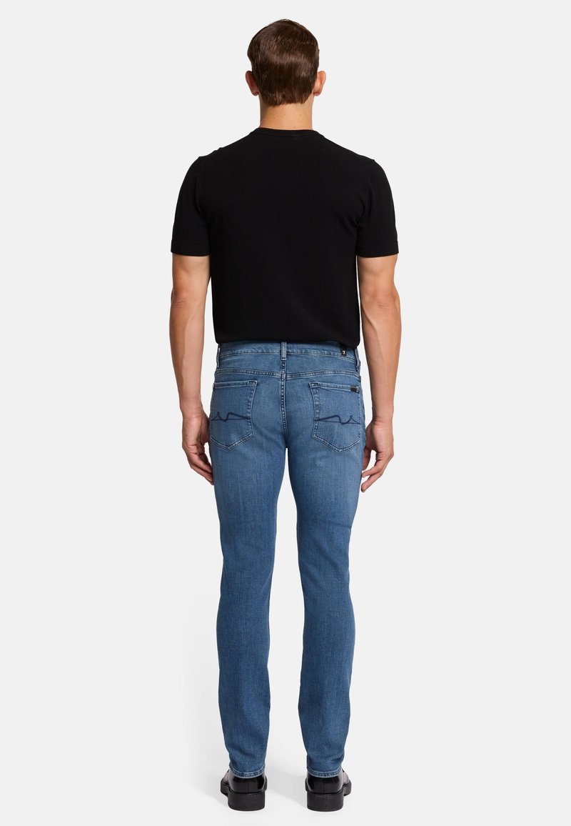 Jeans in denim blu chiaro con vestibilità slim, dotati di due tasche posteriori e dettagli di sorfilatura sottili. Abbinati a una camicia nera a maniche corte.