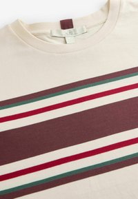 T-shirt en coton beige avec des rayures horizontales bordeaux, rouges, vertes et blanches. Col rond avec une étiquette boucle à l'arrière.