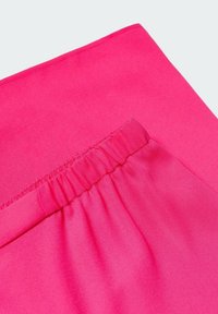 Jasnoróżowa tkanina o gładkiej fakturze, z elastycznym paskiem w talii i detalem bocznej kieszeni. Prosty i minimalistyczny design.