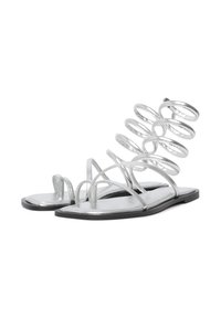 Silberne flache Sandalen mit dünnen Riemchen und spiralförmigem Akzent. Metallisches Finish, offen toe Design und flache Sohle mit minimalem schwarzen Akzent.
