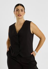 Gilet noir sans manches avec un décolleté en V profond, doté de trois boutons frontaux ornés de nœuds. Texture lisse avec une coupe ajustée.