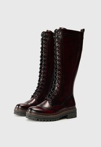 Więzane wysokie buty w głębokim burgundowym kolorze z skóry, z detalami w stylu brogue, ciężką podeszwą oraz metalowymi oczkami na sznurówki.