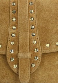 Tan suède tas met een centrale klep met messing studs en een sluiting met een band. De gestructureerde oppervlakte verhoogt de tastbare aantrekkingskracht.