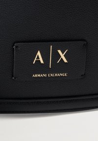 Μαύρο υλικό με υφή, με ραμμένη μαύρη ετικέτα με ανάγλυφα χρυσά γράμματα "A|X" και "ARMANI EXCHANGE".