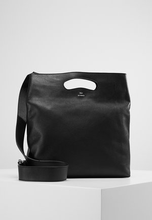 Zwarte leren tote tas met ingebouwde handgreep en afneembare schouderriem, weergegeven op een wit oppervlak tegen een grijze achtergrond.