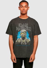 Sort grafisk t-shirt med "Iron Maiden" tekst og en illustreret skelet med kæder og blå lyn accenter. Korte ærmer, afslappet pasform.