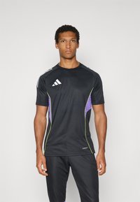 Fekete sportpóló lila és lime zöld részletekkel, rövid ujjú, az Adidas logóval a mellkasán, könnyű anyagból készült.