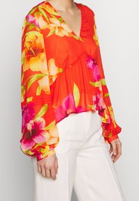 Rode bloes met lange puffmouwen, met levendige gele, roze en oranje bloemen. Lichtgewicht, met een V-hals en een gelaagd ontwerp.