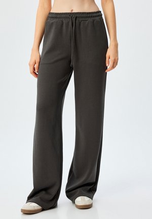 Donkergrijze wijde broek van zacht materiaal, met een elastische tailleband en een trekkoord. Het model draagt beige instappers.
