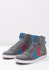 H�øje sneakers i gråt kanvas med blå og røde chevron-detaljer, fremtrædende øjet-huller, flade hvide såler og polstret krave.