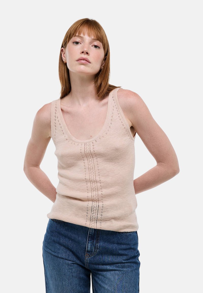 Débardeur en tricot beige avec un décolleté arrondi et des détails verticaux. Associé à un jean en denim bleu taille haute. Texture lisse.