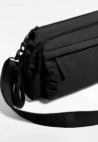 Zwarte nylon schoudertas met meerdere geassorteerde vakken met rits, textuur op het oppervlak, verstelbare schouderband en versterkte stiksels.