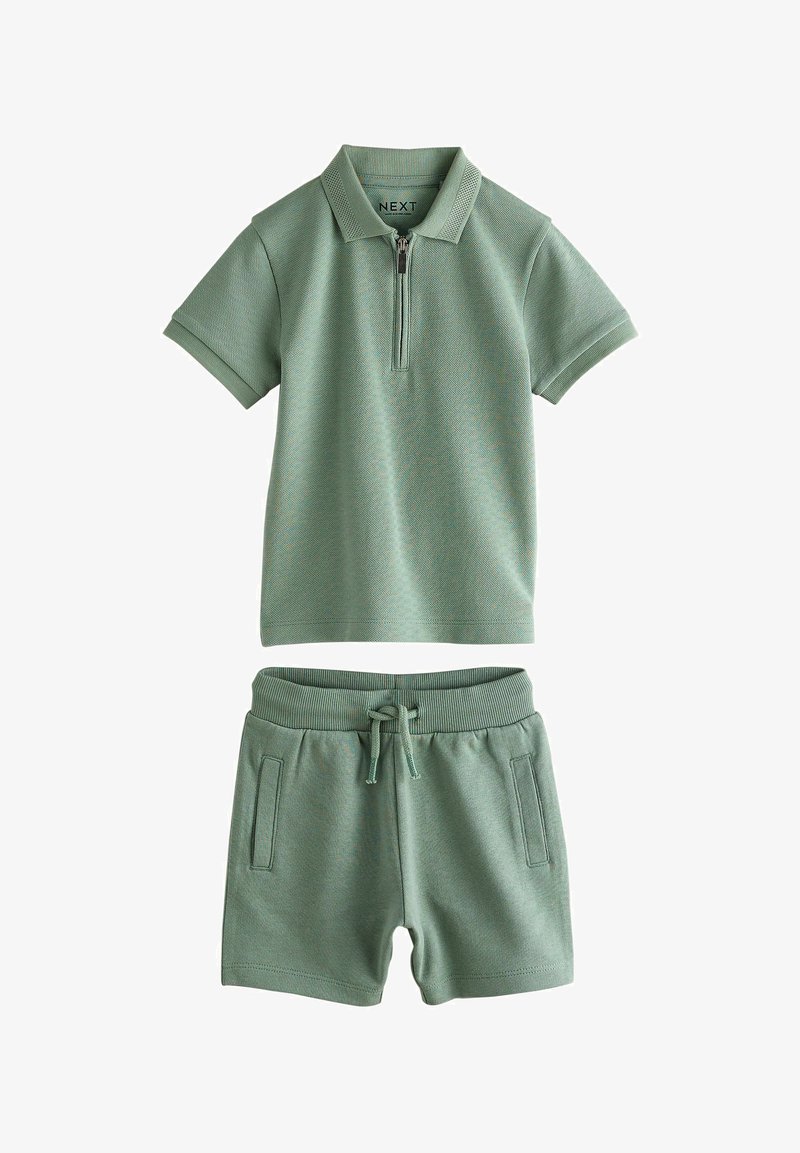 Grünes, kurzärmeliges Poloshirt mit Reißverschluss und passende Shorts mit Kordelzug und seitlichen Taschen, flach auf weißem Hintergrund ausgelegt.