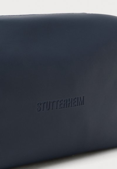 Mørkeblå vandtæt taske med præget "STUTTERHEIM" logo, glat tekstur, afrundet form og minimalistisk design. Ingen ekstra hardware.