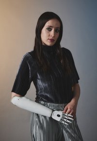 Protetinė ranka su balta apdaila ir metaliniais pirštų sąnariais, derinama su juoda raukšlėta viršutine dalimi ir sidabrinėmis raukšlėtomis kelnėmis.
