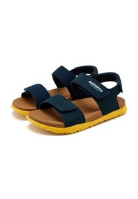 Sandalias de color azul marino con correas de Velcro ajustables, plantillas texturizadas en marrón y suelas de goma amarillas, con detalle del logo en la correa.