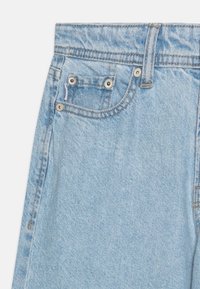 Heled sinine denim teksad, millel on kõrge vöökoht, viie tasku disain ja nähtavad õmbluse detailid. Kangas on pehme ja tekstureeritud viimistlusega.