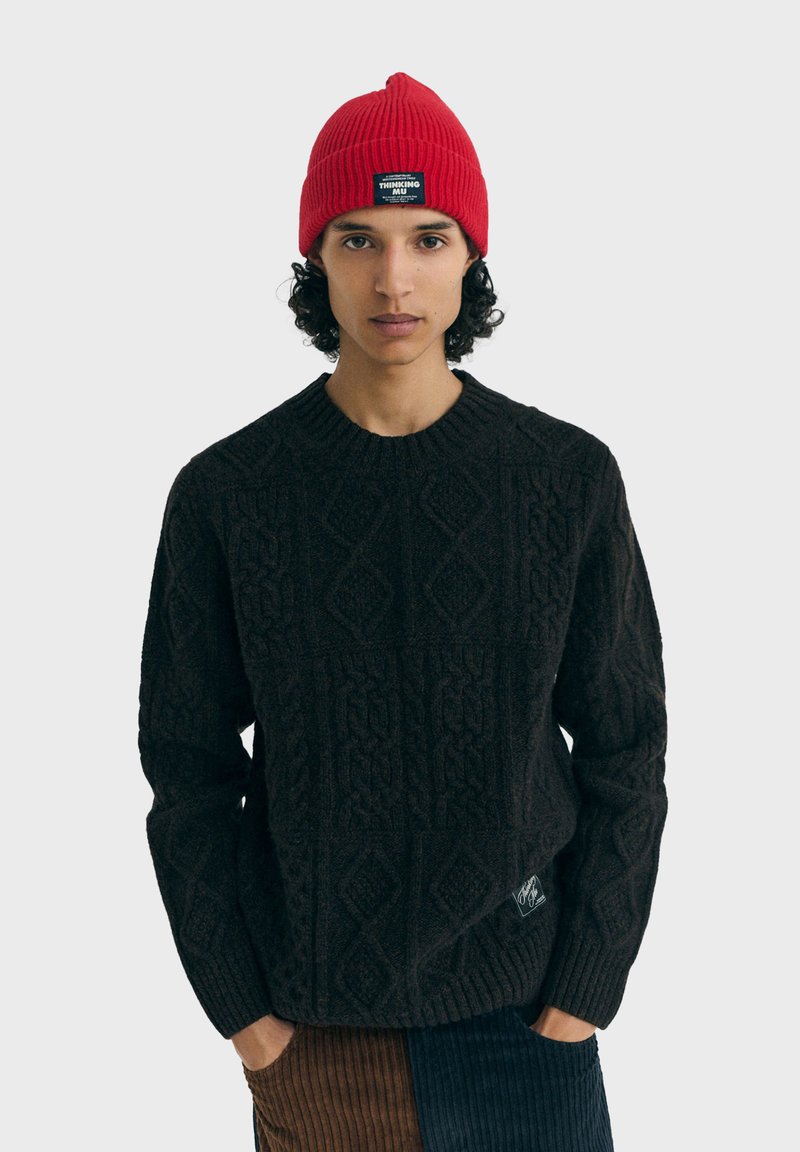 Pull en maille noire avec un motif en diamant texturé, col et ourlet côtelés. Associé à un bonnet rouge côtelé avec un écusson logo.