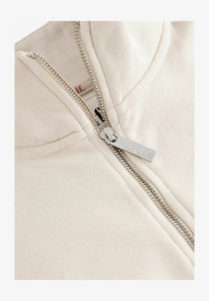 Beige Kapuzenjacke mit silbernem Reißverschluss und einem Marken-Zipper. Hergestellt aus einem Baumwollmischgewebe mit glatter Textur.