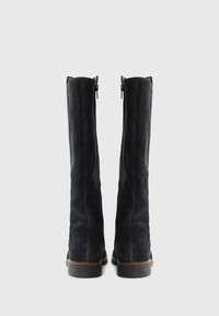 Bottes noires en suède, hauteurs de genoux, avec des fermetures éclair sur le côté, semelles plates et finition texturée. Présente un design simple et des coutures marron contrastantes.