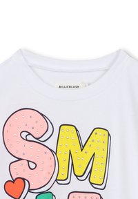 Weißes T-Shirt mit großen bunten Buchstaben "SM", verziert mit kleinen Strasssteinen und einem roten Herzdetail neben dem Buchstaben "S".