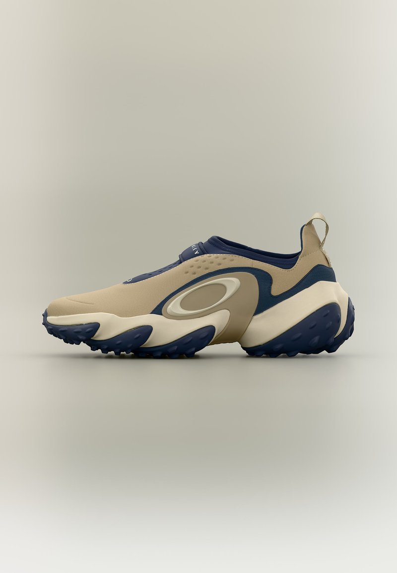 Μπεζ και μπλε ναυτικό αθλητικό παπούτσι slip-on με υφασμένο πάτο, θηλιά στο τακούνι και κυματιστά σχέδια στο πλάι και στη μέση της σόλας.