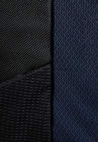 Svart texturerad tyg kontrasterar med mörkblå mönstrat material, som har en geometrisk design och varierande ytkvaliteter.