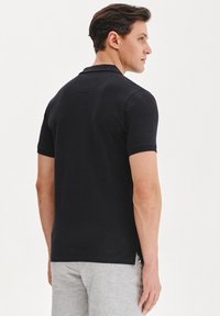 Czarna koszulka polo z krótkimi rękawami, klasycznym kołnierzykiem i prostym dołem. Materiał wydaje się gładki, z minimalnymi detalami.