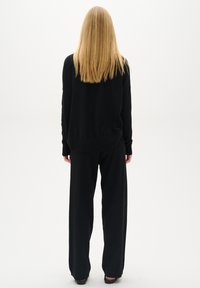 Schwarzer Strickpullover mit lässiger Passform, kombiniert mit passenden weiten Hosen. Glatte Textur und schlichtes Design, von hinten betrachtet.
