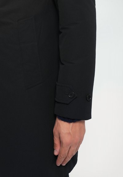 Schwarzer Mantel mit langen Ärmeln aus strukturiertem Stoff, mit einem geknöpften Manschette und einer Tasche am Ärmel. Schlichtes, minimalistisches Design.