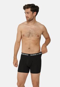 Svarta boxershorts med tajt passform, med ett vitt elastiskt midjeband märkt "DANISH ENDURANCE." Mjukt tyg och längd till mitten av låret.