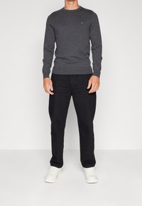 Grå tröja med rund halsringning, ribbad mudd och nederkant, kombinerad med svarta byxor och vita sneakers. Logotyp som syns på tröjan.