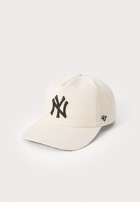 Casquette de baseball crème avec un logo NY noir brodé à l'avant et une petite marque ’47 sur le côté. Présente une forme structurée et un bord plat.