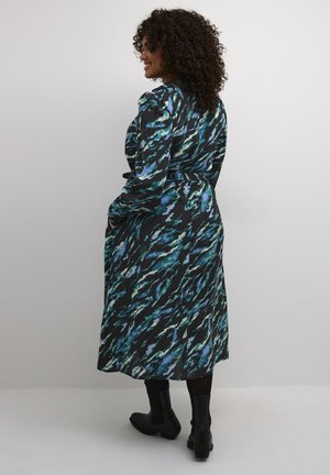 Langärmliges, knielanges Kleid mit schwarzem Grund und abstraktem Muster in Blau und Türkis. Kombiniert mit schwarzen Stiefeletten aus strukturiertem Material.