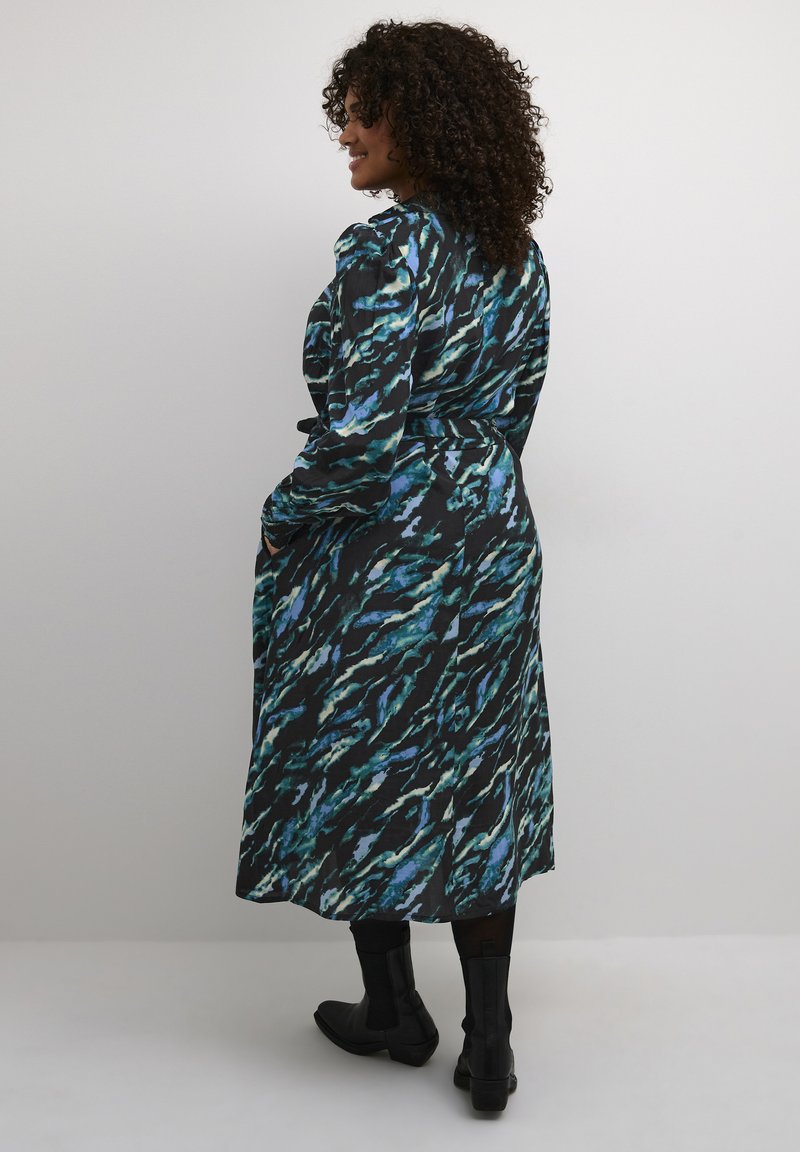 Rochie cu mânecă lungă, de lungime medie, ce prezintă o bază neagră cu un model abstract în nuanțe de albastru și teal. Asortată cu bocanci negri până la glezna, din material texturat.