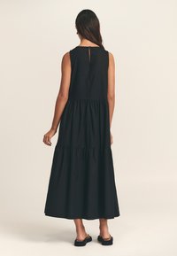 Juoda maksi suknelė su sluoksniuota konstrukcija, be rankovių, su skylute nugaroje. Pagaminta iš lengvos medžiagos, pasižymi laisvai krintančia siluetu.