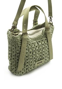 Bolso de mano de ganchillo verde con acentos de correa de cuero, que cuenta con un compartimento con cremallera y un diseño texturizado y tejido. Etiqueta de la marca visible.