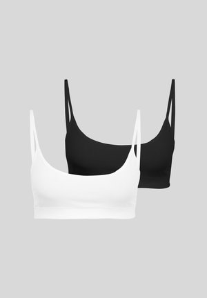 Két varrás nélküli bralette, egy fehér és egy fekete, vékony pántokkal, sima szürke háttéren.