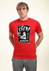 Rød bomulds T-shirt med et sort-hvidt grafisk print med teksten "ALIEN INVASION." Kortærmet og design med rund hals.