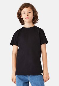 Sort bomulds-T-shirt med korte  ærmer, rund halsudskæring og et lille mærke på siden. Kombineret med blå denimjeans.