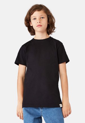 Sort bomulds-T-shirt med korte ærmer, rund halsudskæring og et lille mærke på siden. Kombineret med blå denimjeans.