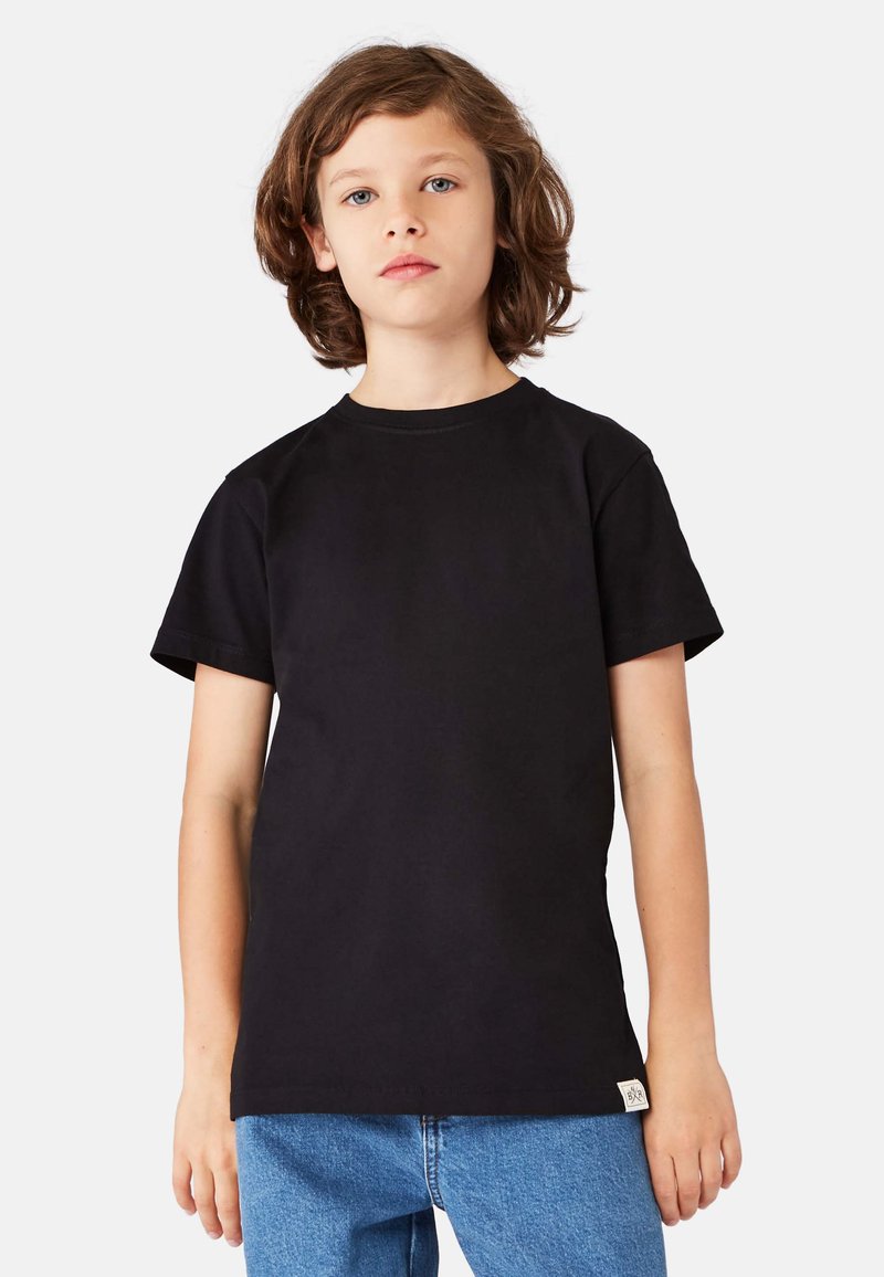 Sort bomulds-T-shirt med korte ærmer, rund halsudskæring og et lille mærke på siden. Kombineret med blå denimjeans.