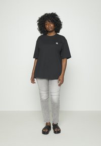 T-shirt oversized de algodão preto com um logótipo branco, combinado com jeans cinzentos ajustados com costura lateral e sandálias pretas.