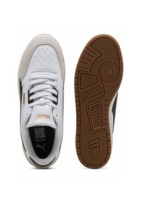 Baskets blanches avec des accents noirs et bruns, tige en cuir lisse, bout perforé, lacets plats, et semelle en caoutchouc brun texturé avec logo.