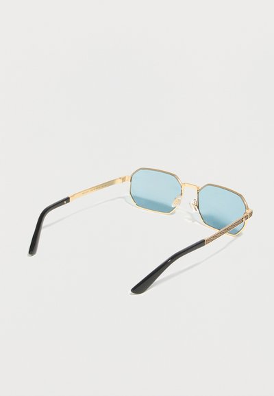 Γυαλιά ηλίου με χρυσή κορνίζα, φωτεινούς γαλάζιους εξαγωνικούς φακούς και μαύρες άκρες στα κέρατα, απεικονίζονται σε απλό λευκό φόντο.