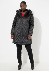Cappotto imbottito lungo nero, con zip e chiusura a scatto, cappuccio e tasche laterali. Presenta una texture lucida e liscia e un fit leggermente oversize.