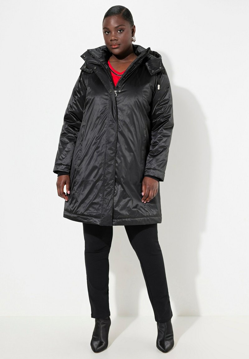 Cappotto imbottito lungo nero, con zip e chiusura a scatto, cappuccio e tasche laterali. Presenta una texture lucida e liscia e un fit leggermente oversize.