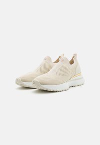 Beige slip-on sneakers laget av teksturert mesh-stoff; hvit gummisåle med en subtil gyllen aksent. Lett og pustende design.