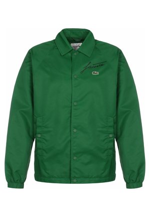 Grüne Lacoste-Jacke mit Knöpfen, elastischen Bündchen, zwei Seitentaschen und schwarzem Schriftzug mit Krokodil-Emblem auf der Brust.