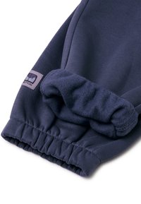 Puño de sudadera azul marino con un interior de felpa suave, banda elástica y un pequeño parche de logo en forma rectangular.